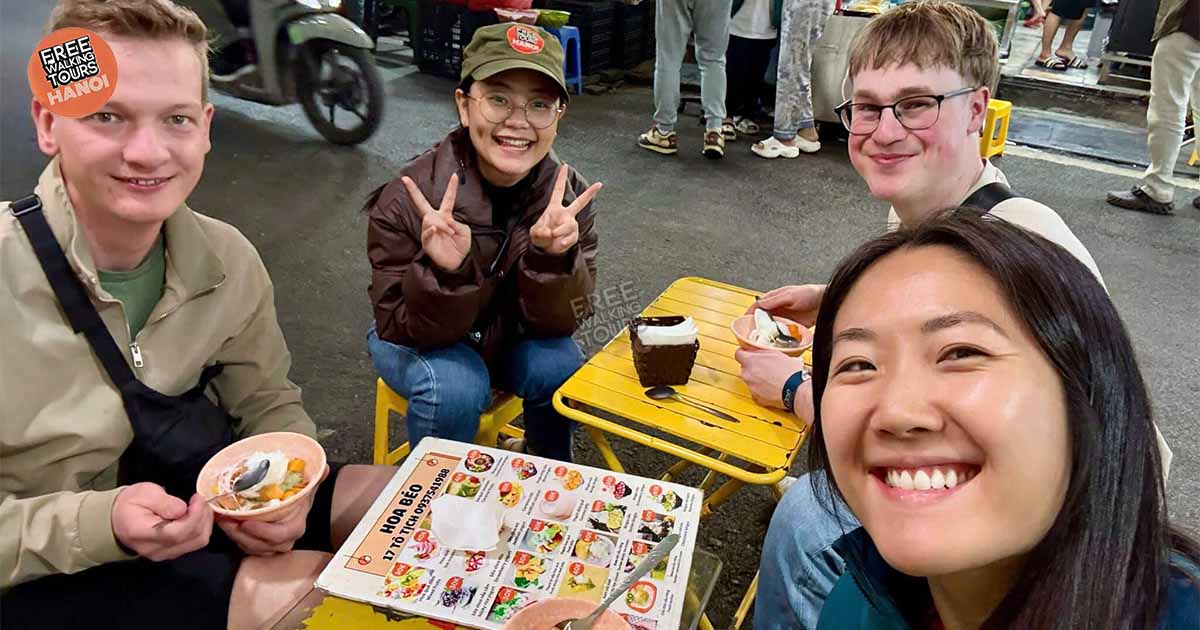 Tourists enjoying Vietnamese street food with local guide at Hanoi’s bustling night market